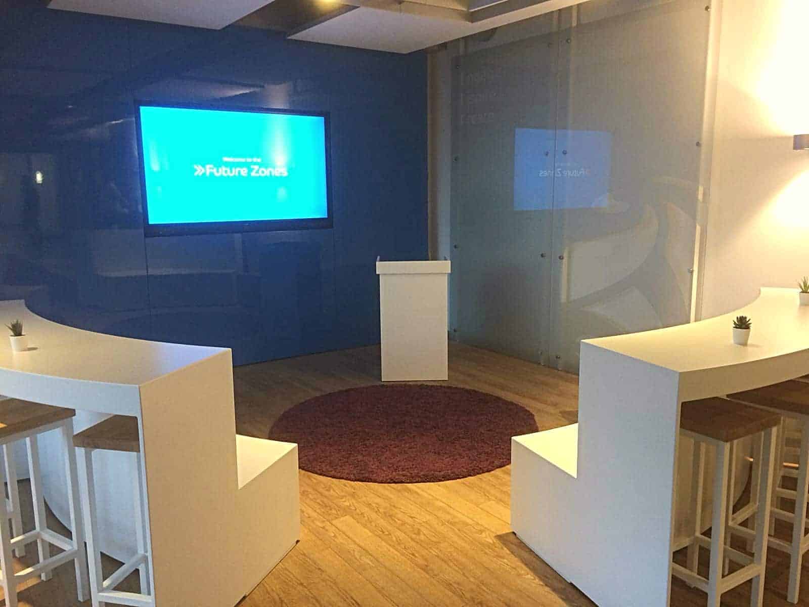 Idea Station at the Barclaycard Hamburg headquarters with a 75-inch Philips touch monitor on a blue wall, a white presentation lectern and curved white bench seating
