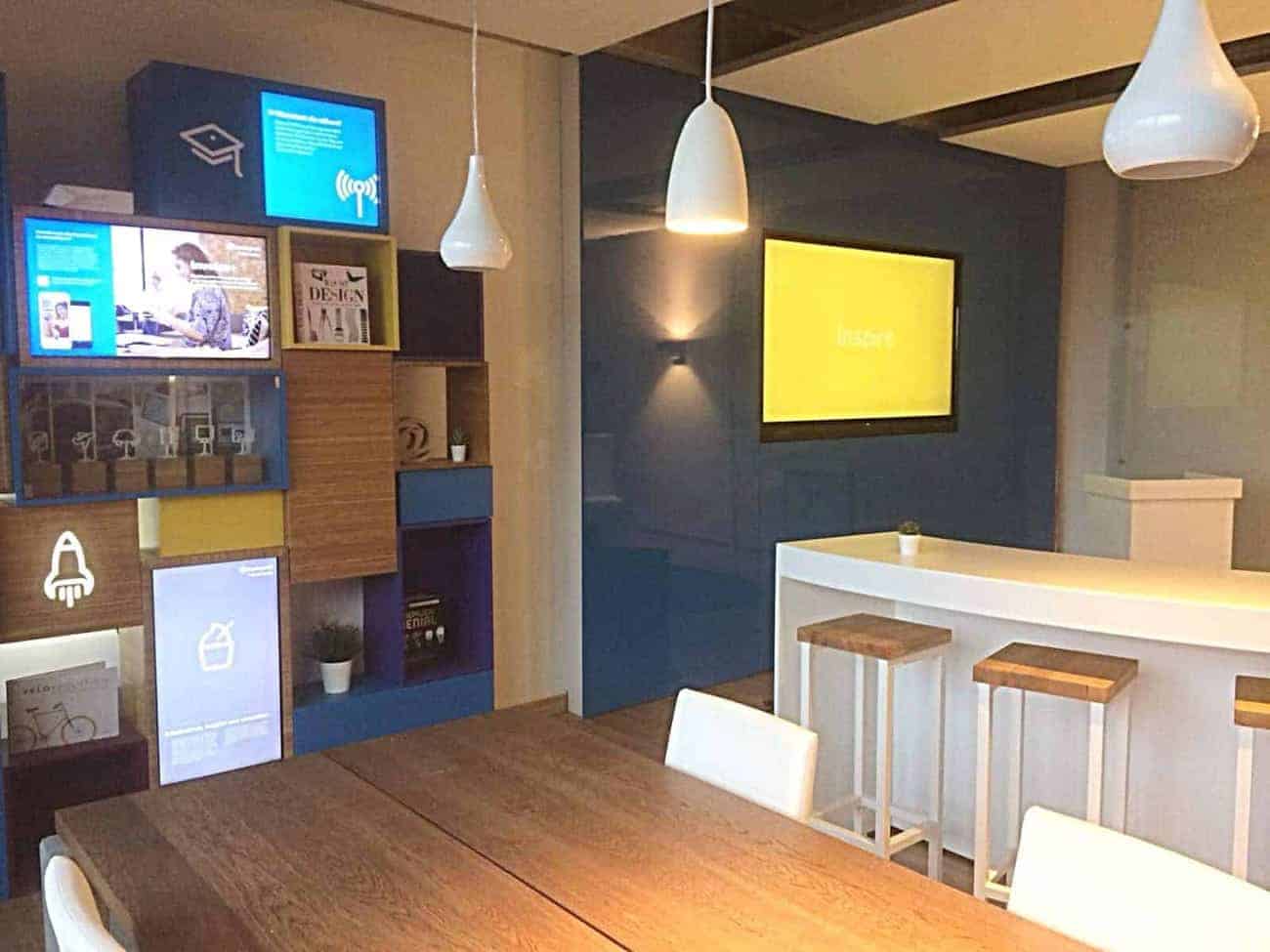 Second view of the Barclaycard Hamburg digital bookcase with a wall-mounted monitor showing the word Inspire above a white breakfast bar