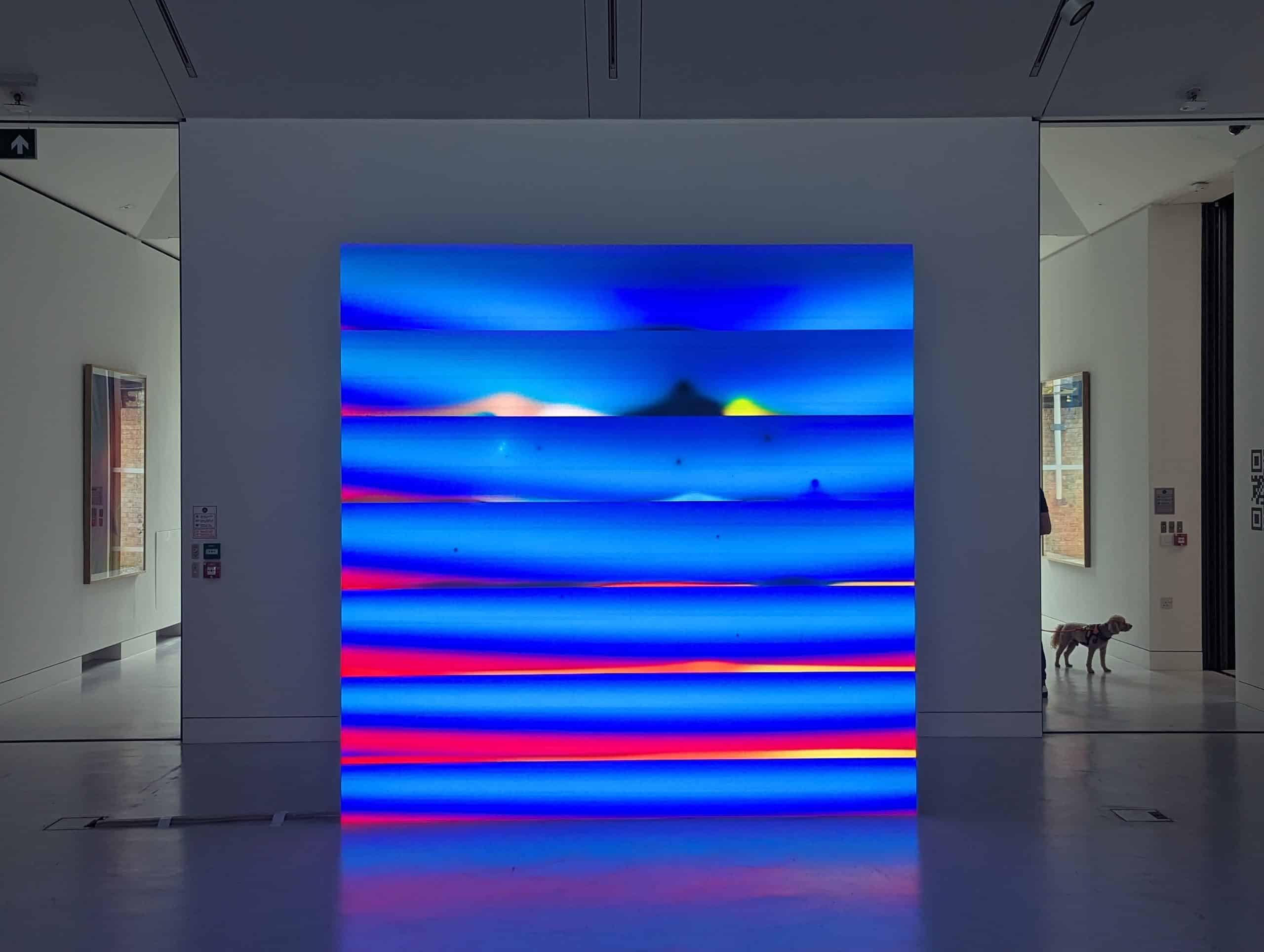 Zach Lieberman blue and red generative artwork on a free-standing Dynamo LED screen in the darker second room at Verse gallery, London, with framed works on the side walls