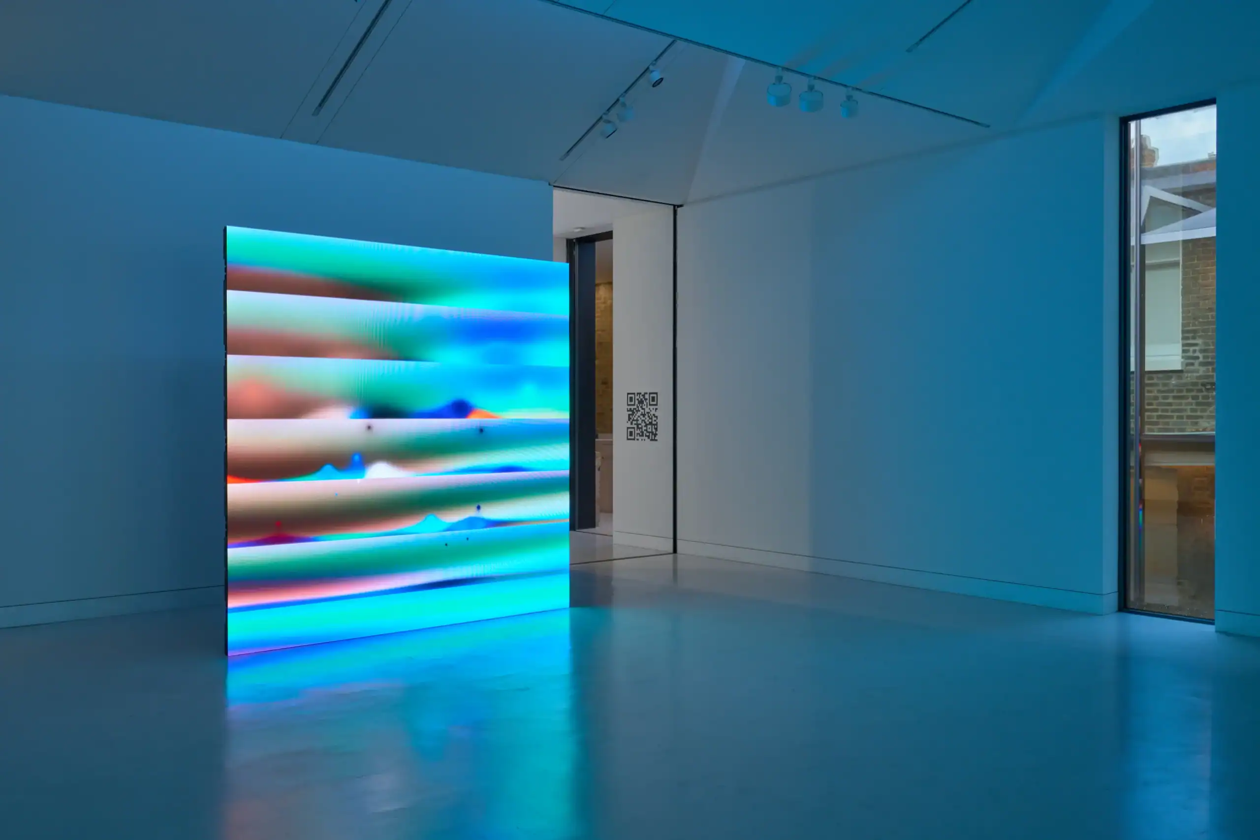 Dynamo LED screen showing a Zach Lieberman green and blue banded artwork in a blue-lit room at Verse gallery, London, with a QR code on the wall beside the doorway