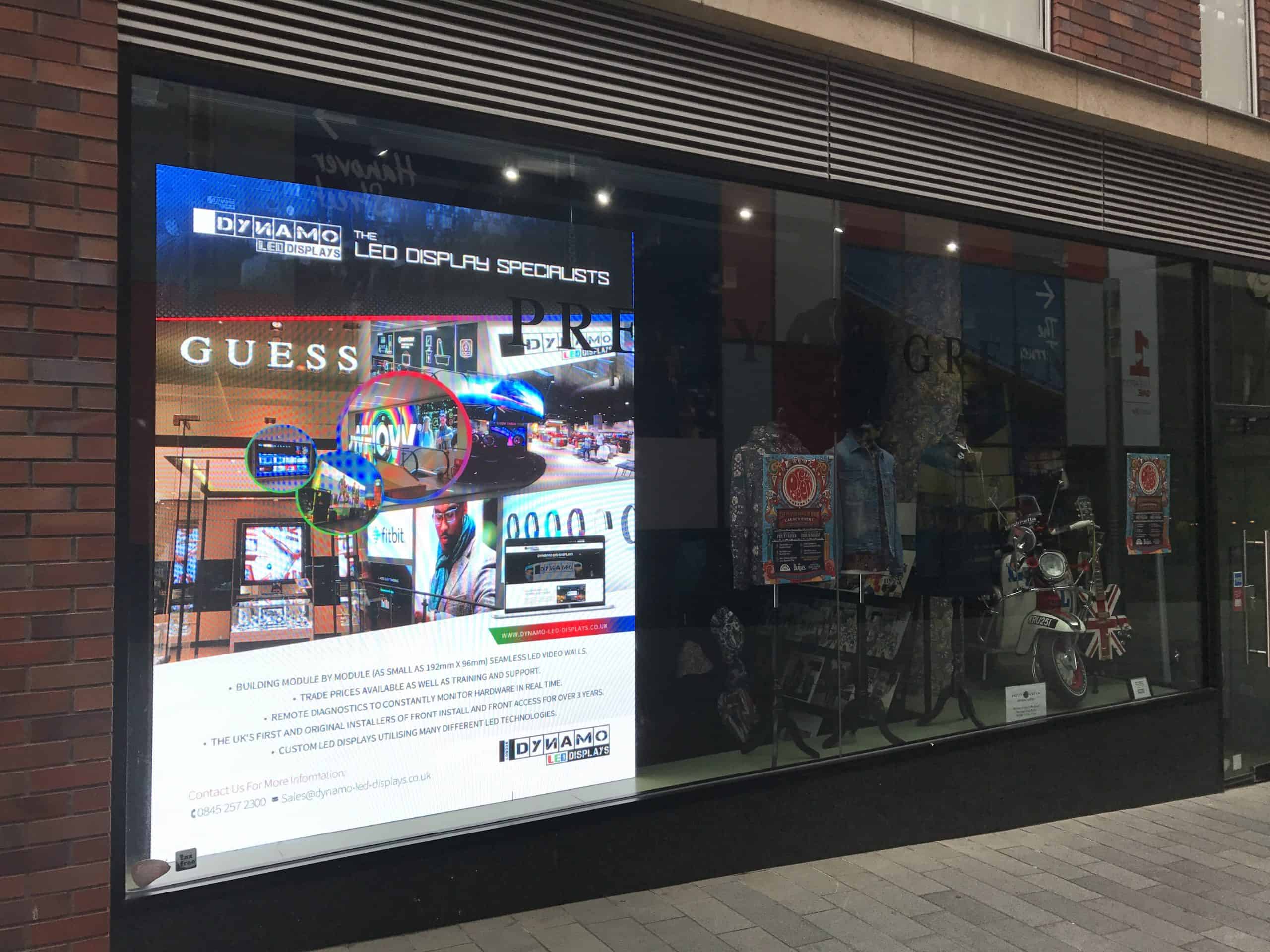 Pretty Green store window with a high-brightness 2.6 mm LED screen behind the glass showing a Dynamo LED Displays advert, beside mannequins and a scooter in the window display