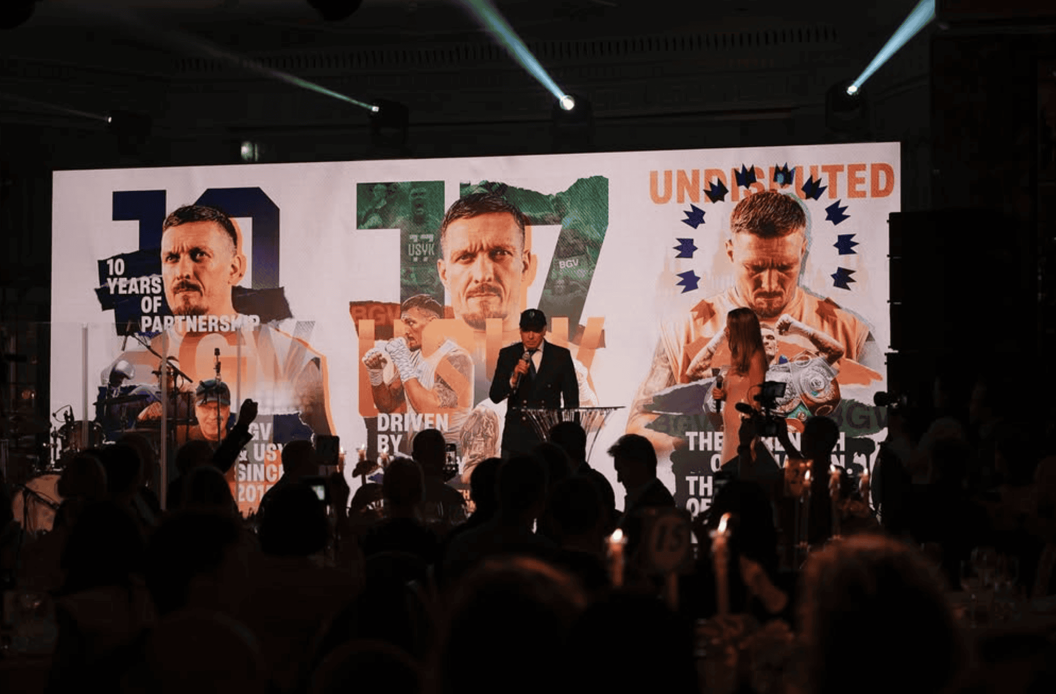 Speaker at a lectern in front of the 7 m LED screen at the Usyk gala showing a 10 Years of Partnership and Undisputed sponsor artwork with images of Oleksandr Usyk