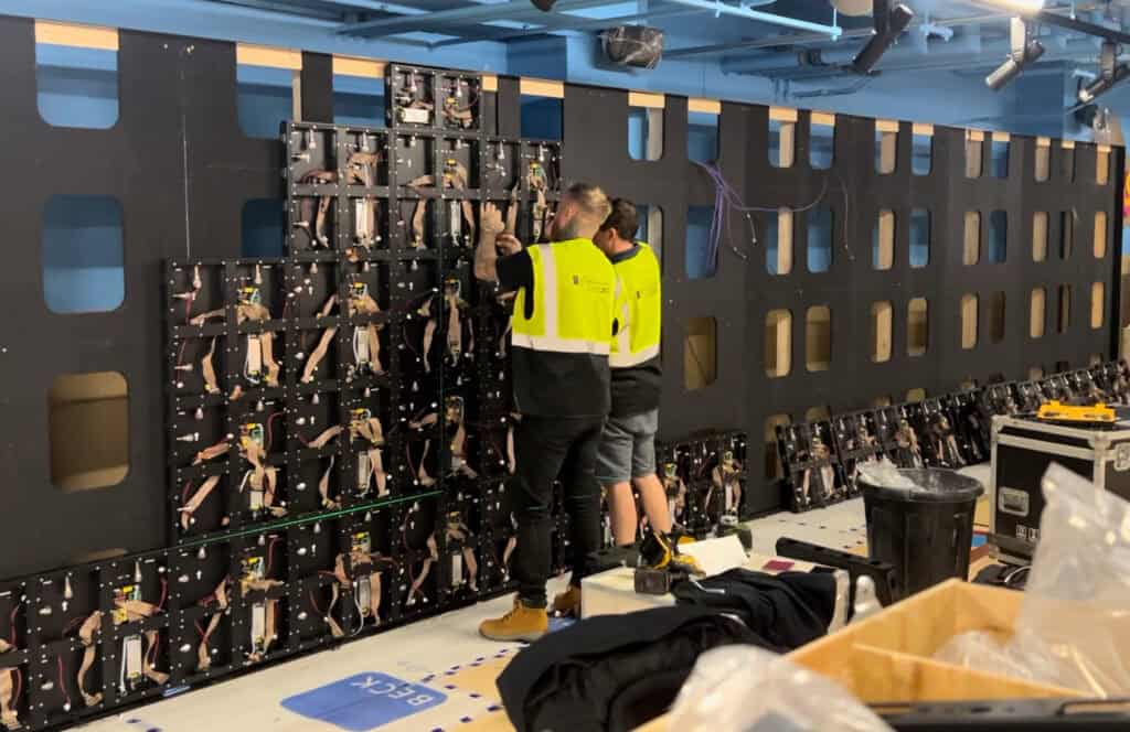 Technician servicing a wall-mounted LED display from the front.