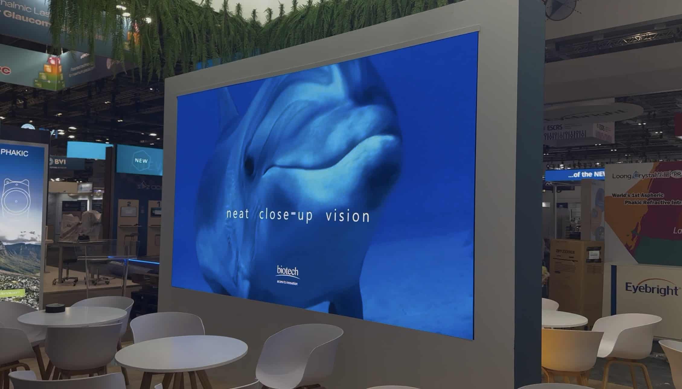Freestanding 3 m x 2 m 1.29 mm LED booth wall inside the Biotech stand at ESCRS 2026 showing dolphin content, neat close-up vision