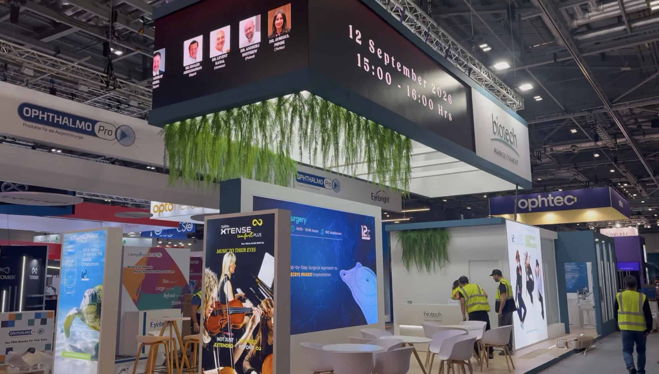 Two faces of the hanging LED banner over the Biotech stand: speaker headshots on the long run, the 12 September session slot on the return