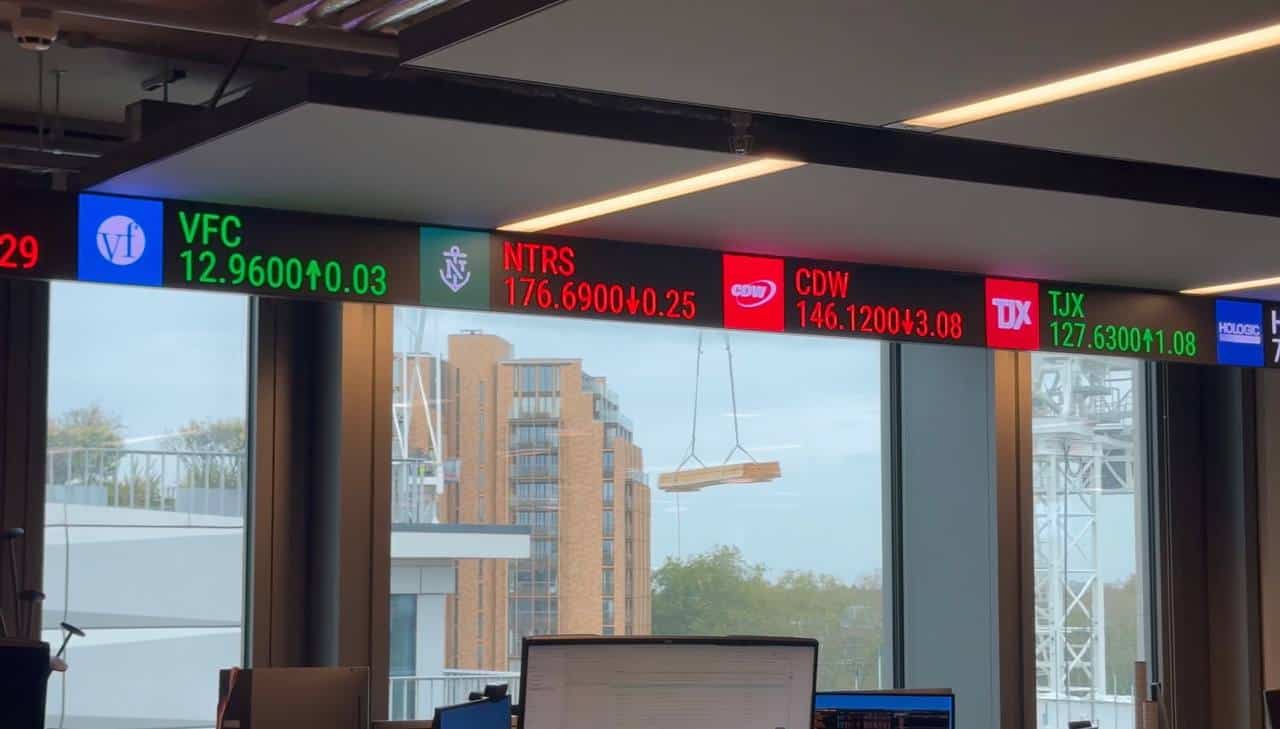 Trading floor LED ticker in its ceiling-line housing above the window wall at 25 Baker Street, with construction on Baker Street beyond